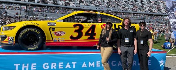 students from sales program posing next to yellow NASCAR car number 34